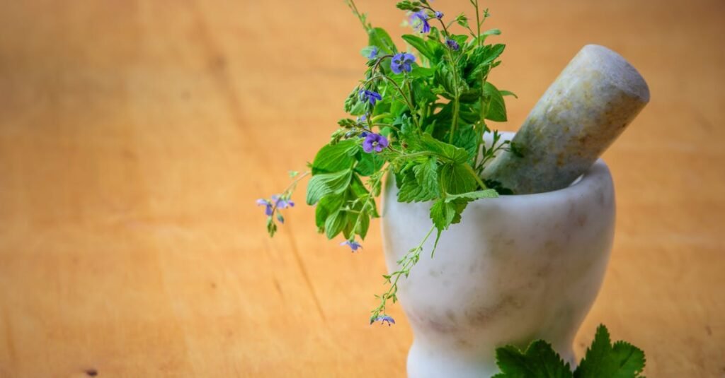 Marble mortar and pestle with fresh herbs and flowers on wooden table enhancing natural health and cooking aesthetics.