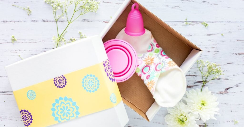 Brightly decorated gift box containing reusable menstrual cup and pads on a rustic background.