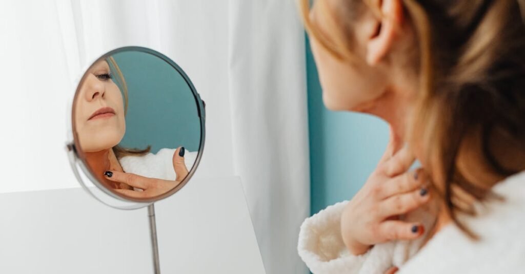 Woman in a bathrobe applying skincare while looking in the mirror.